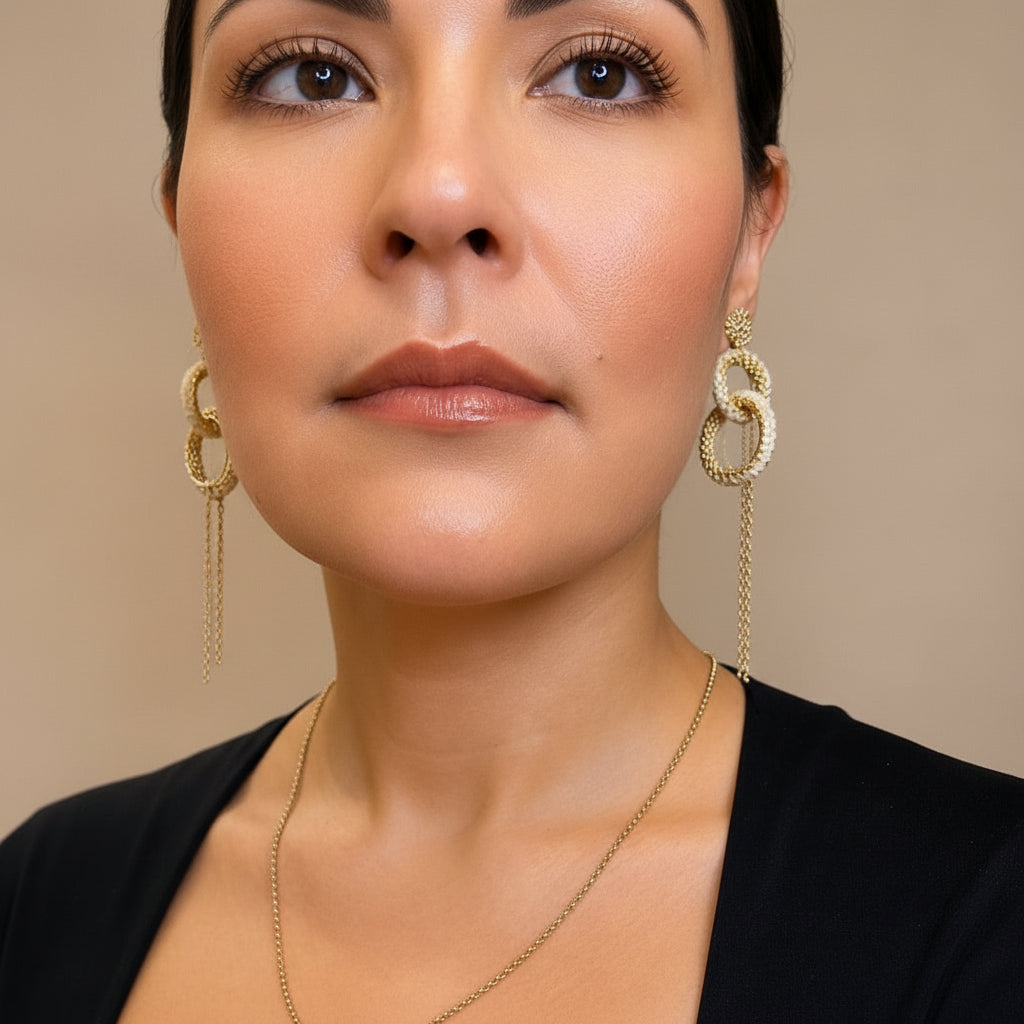 Woman wearing gold chain earrings and a necklace against a neutral background